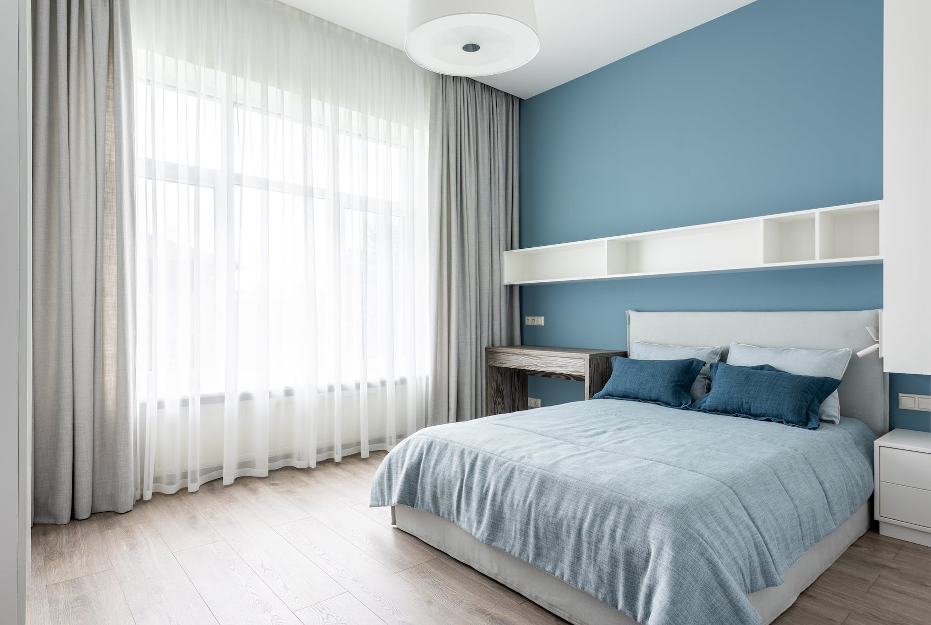 Blue hue Day and Night curtains in contemporary bedroom with soft bed and blue pillows