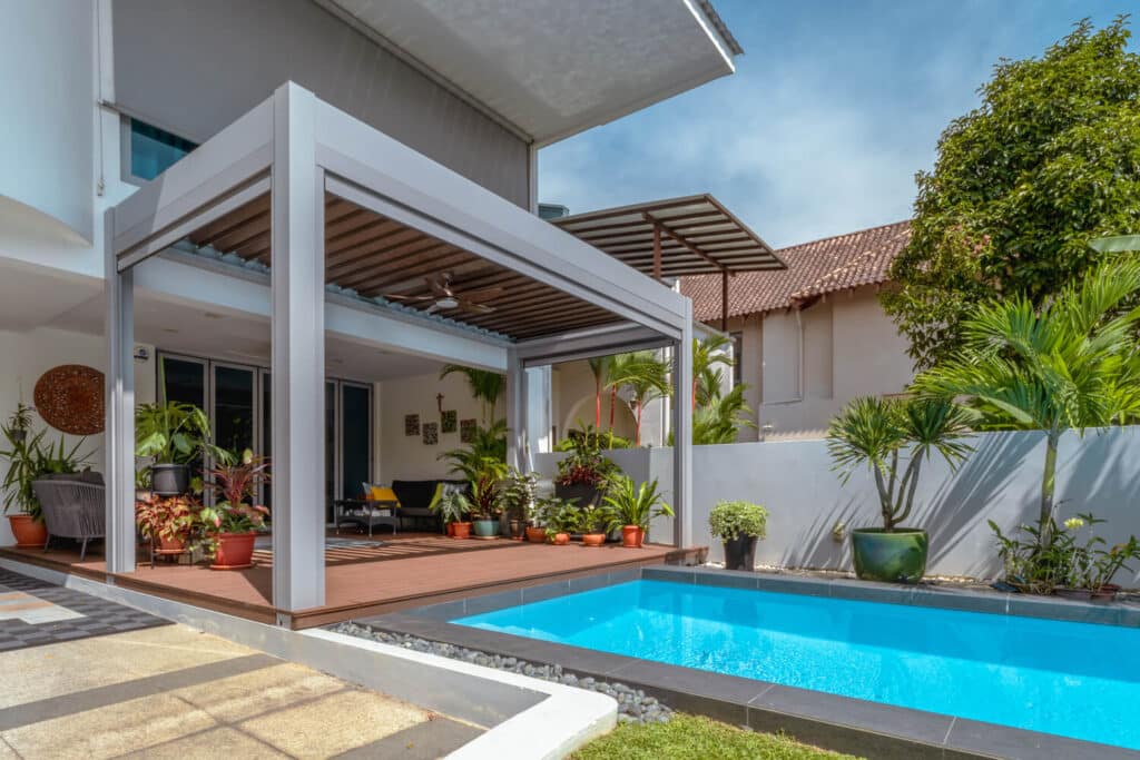 Luxurious outdoor space featuring a louvered pergola with adjustable slats, a cozy seating area, and tropical plants, set beside a sparkling swimming pool.